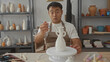 © Krakenimages.com - Young chinese artisan man brushes glaze onto glossy white ceramic vase on rotating pottery wheel in studio; focus.