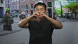 © Krakenimages.com - Smiling man forming heart gesture with hands in urban pedestrian street scene with blurred passersby; love.