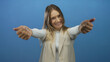 © Krakenimages.com - Smiling young blonde woman in a white shirt and beige vest gesturing over isolated blue background wall, conveying happiness and friendliness.