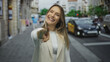 © Krakenimages.com - Woman happily pointing at camera on busy city street with blurred traffic and buildings, capturing a candid moment outdoors.