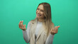 © Krakenimages.com - Young blonde woman gesturing money with fingers against isolated green background wall, expressing concept of wealth and success.
