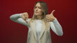 © Krakenimages.com - Woman with thumbs up and down gesture smiling against a vibrant red backdrop displaying mixed emotions highlighting decisionmaking and expression.