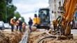 © Laura - Faceless construction workers and heavy machinery laying underground fiber optic cables in a trench at a road construction site, defocused background, high-speed internet