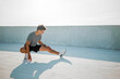 © muse studio - Man stretches on an outdoor surface during daytime for fitness activity in a city setting