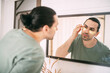 © Anna - Spa day at home. Young man with patches under his eyes at the mirror at home.