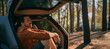 © Anna - A young man is sitting relaxed alone in the open trunk of a car in the woods by the lake at sunset.