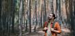 © Anna - Portrait of a young man with a backpack on a walk in a pine forest on a sunny day. The guy breathes fresh air in a coniferous forest