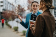 © qunica.com - Two colleagues discuss ideas on a city sidewalk, with one woman gesturing and holding documents. A professional in a blue coat chats with a partner in an urban street setting.