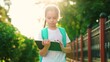 © Victoriia - Girl student returning home from school after lessons. Child with backpack tablet. Charming child schoolgirl walks city street after school uses digital tablet. Mobile gadget in hands child outdoors