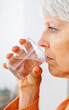 © Xavier Lorenzo - Vertical shot. Close-up side view of senior woman drinking water from glass at home. Healthy lifestyle concept.