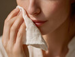 © Promsiri - Woman hand holding soft white cloth gently blotting face, close up of skincare routine, natural light, healthy skin, self care, relaxation, morning beauty ritual