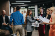 © qunica.com - A group of professionals exchange documents and discuss in a busy, modern office.