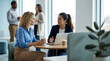 © Creative Spectrum - Two professional women discussing work over coffee with a laptop at a round table in a contemporary office setting