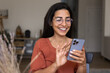 © fizkes - Cheerful woman in glasses exchanges messages with friend using mobile application on smartphone on weekend rest at home, smile, typing sms, makes call to family, enjoy new AI platform for fun or hobby