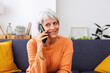 © Xavier Lorenzo - Elegant senior woman with short gray hair having a pleasant phone call with friend while sitting on a comfortable sofa in her living room