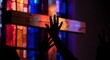 © Yuliia - Silhouette of hands reaching toward illuminated stained glass cross in dark church interior creating spiritual worship atmosphere for religious content.