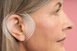 © New Africa - Hearing health. Senior woman with audio waves around her ear on pink background, closeup