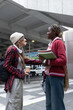 © wavebreak3 - Diverse female students chatting under overpass in beanie and red jacket holding coffee and folders