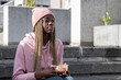 © wavebreak3 - African American woman sitting on urban steps in pink beanie, holding plastic container with fork
