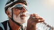 © Joyce - Cardio sports cycling biking exercise training, healthy lifestyle. An elderly man wearing a helmet and sunglasses, drinking water from a bottle. The background is slightly blurred.
