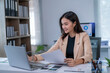 © Wasana - Young professional checking paperwork and working on a laptop in her modern office
