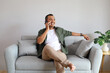 © ArvStd - A contented adult man is talking on his cell phone while relaxing on the sofa at home, looking out the window at the yard.