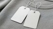 © EDI - Close-up of two blank white tags with strings on a gray fabric surface, ready for text.
