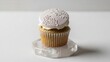 © Soeb Kaes - Elegant vanilla cupcake with white frosting and delicate white snowflake pattern decoration, presented on a clear hexagonal crystal base against a bright white background