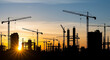 © YourStock - Silhouette of multiple construction cranes and unfinished buildings against a vibrant sunset sky symbolizing development and urban progress with dramatic backlighting