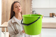 © Pixel-Shot - Worried young woman placing green bucket under water dripping from ceiling in kitchen
