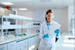 © we.bond.creations - Female scientist wearing safety glasses and lab coat, smiling while analyzing data on a tablet in a modern research laboratory