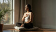 © pantarwat - A woman practices mindfulness meditation by the window, focusing on relaxation and self-care in a serene home environment.