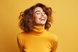 © juliars - Happy young woman with curly hair wearing a yellow turtleneck laughing cheerfully on a yellow background