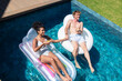 © Wavebreak Media - Diverse couple in swimwear floating on lounge, round float in pool holding citrus drinks and hands