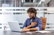 © Tetiana - A young Indian man, twisted in pain, sits in an office at a desk with a laptop and holds his hand to his chest