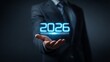 © Adobe - A businessman in a suit holding the year 2026 in his hand with a glowing blue neon effect