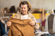 © JackF - Adult man in coat choosing brown pants in a clothing store with a counter in the background. Buying trousers on sale