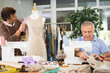 © JackF - Experienced tailor sews clothes against the background of his assistant, who checks a sample of the dress on a mannequin. Male tailors work on ordering clothes in the workshop