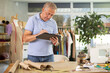 © JackF - Mature man dressmaker draws pattern on tablet in sewing workshop