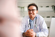 © Studio Marmellata - A smiling doctor in a white coat with a stethoscope listens attentively to a patient during a consultation in a bright, modern office.