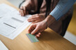 © Studio Marmellata - A man's hand offers a credit card to a woman who is reviewing documents at a desk, suggesting a transaction or payment.