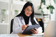 © Studio Marmellata - A smiling woman in a lab coat uses a stylus to write on a tablet computer while working at her desk.