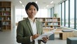 © MopoWe - Young asian professional male smiling holding an open inspire notebook in a bright modern library environment