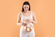 © New Africa - Choosing name for baby. Pregnant woman with pen and notes on her belly against orange background
