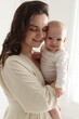 © New Africa - Smiling mother in dress holding her cute baby near white wall at home
