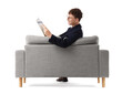 © Pixel-Shot - Redhead young businessman reading magazine on grey sofa against white background, back view