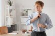 © Pixel-Shot - Young redhead businessman adjusting necktie in office