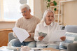 © Pixel-Shot - Senior couple with refund forms and money sitting on sofa at home