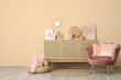 © Pixel-Shot - Interior of stylish room with pink armchair, wicker ottoman and home decor on commode near beige wall