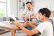 © Pixel-Shot - Teenage boy showing paper sheet to his father and wind turbine models on table at home